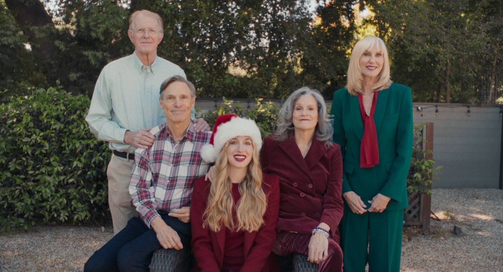 Lydia in a Santa hat sits for a Christmas card photo surrounded by her four parents in a Studio City backyard.