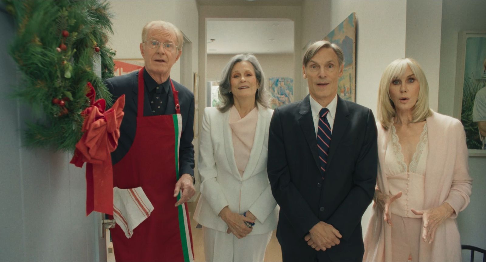 Four parents crowd a front doorway hung with a Christmas wreath, looking startled.