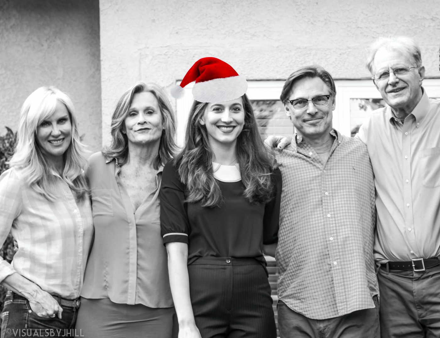 Black-and-white photo of Elizabeth Guest, wearing a red Santa hat, arm in arm with four cast members outside a house.